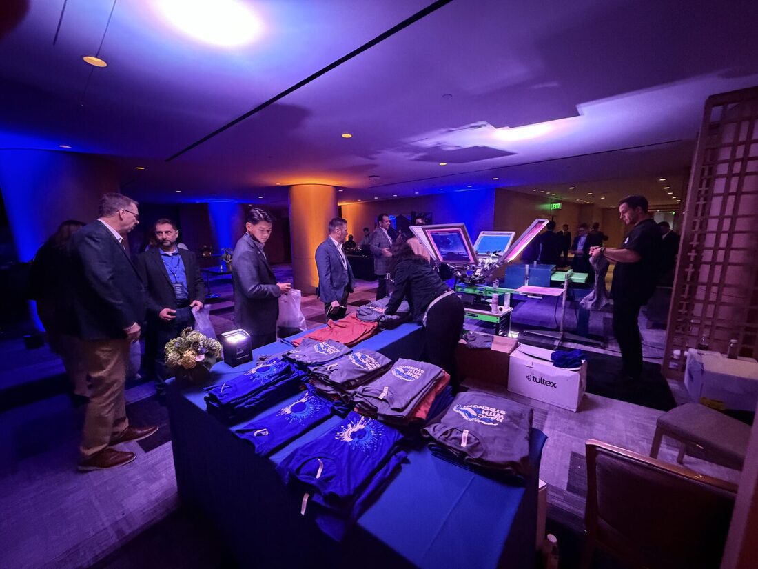 Guests browsing folded custom-printed shirts and totes at a moody, blue-lit evening event